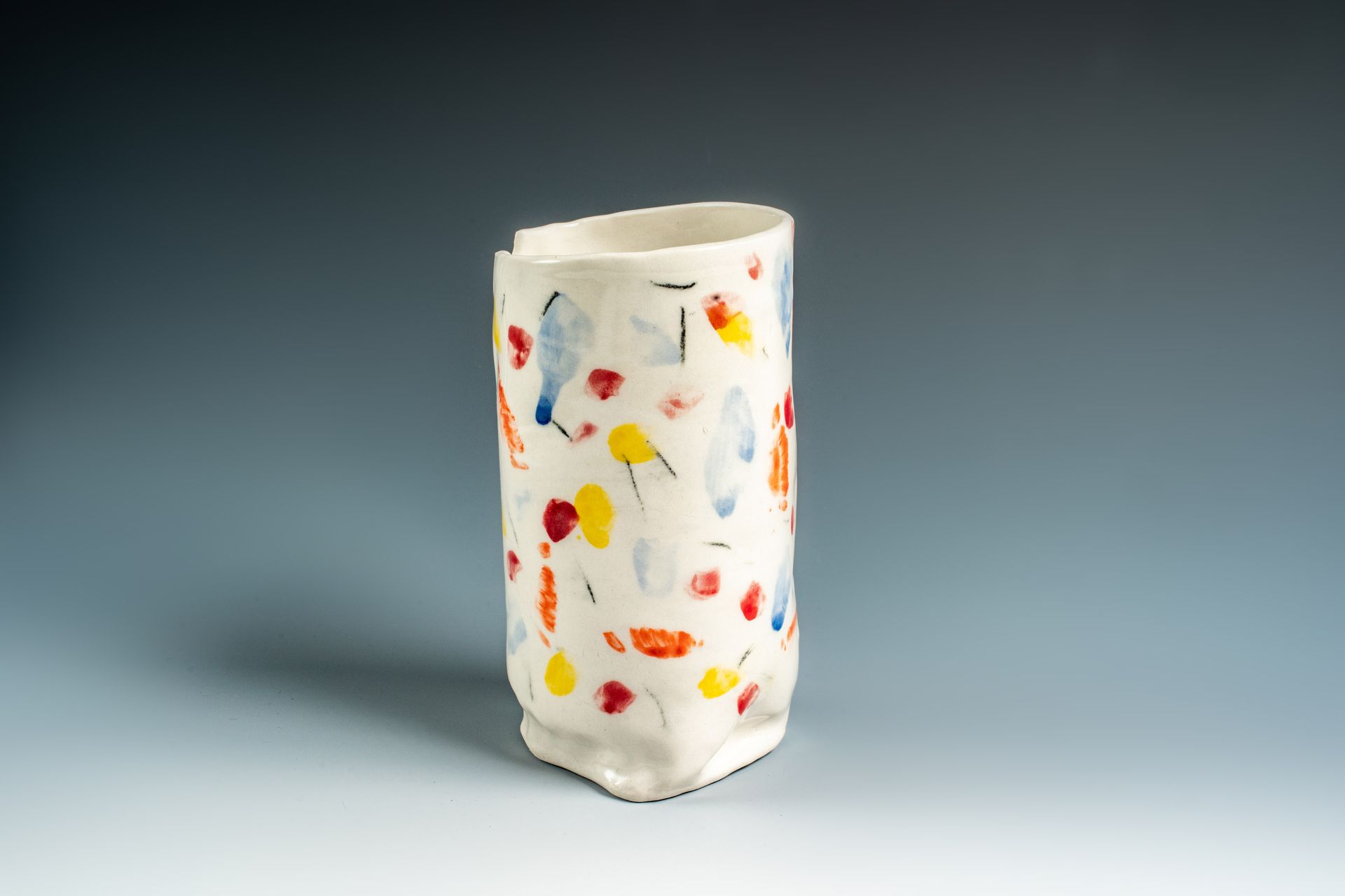 A white vase with colorful spots on it is sitting on a table.