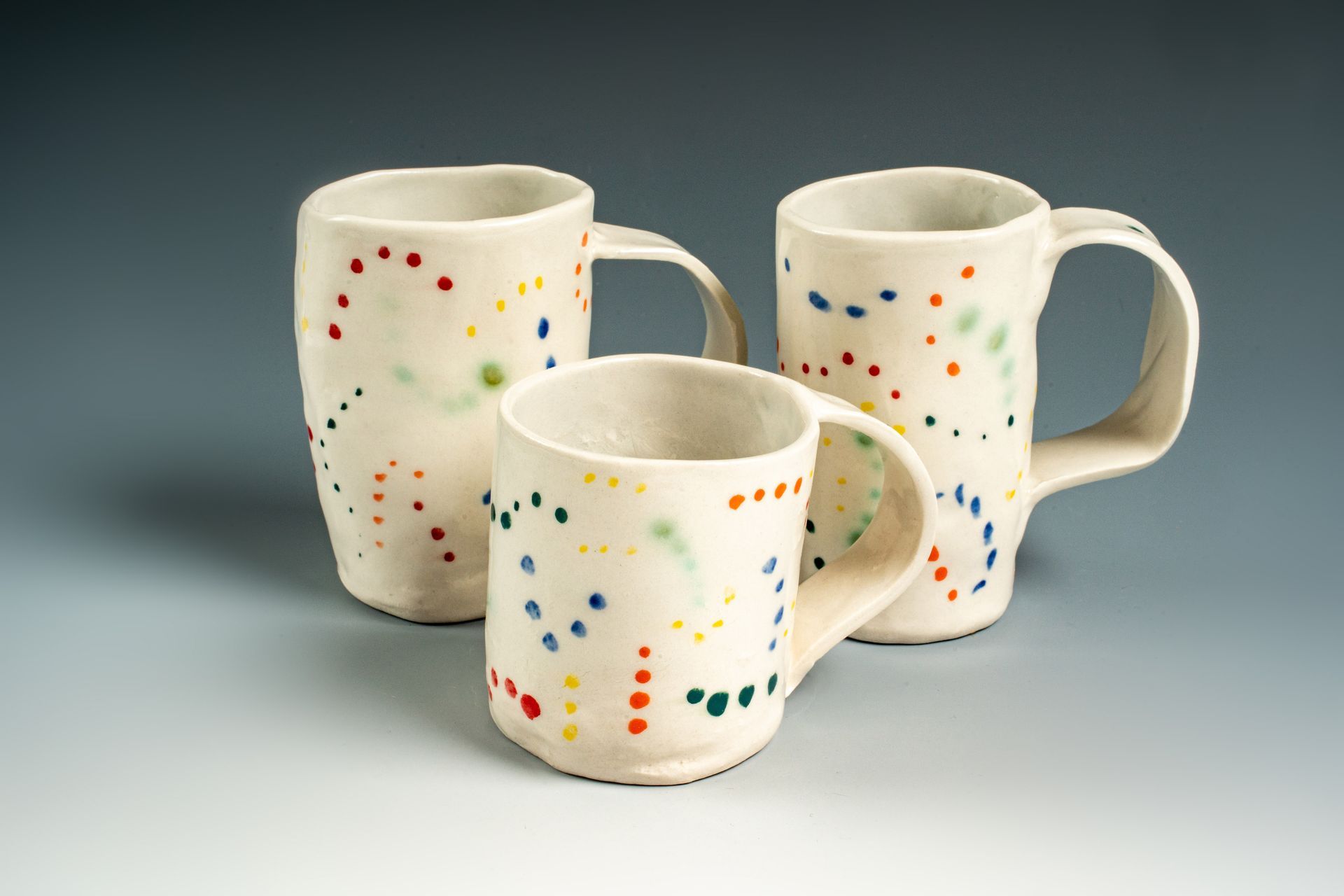 Three white mugs with polka dots on them are sitting on a table.