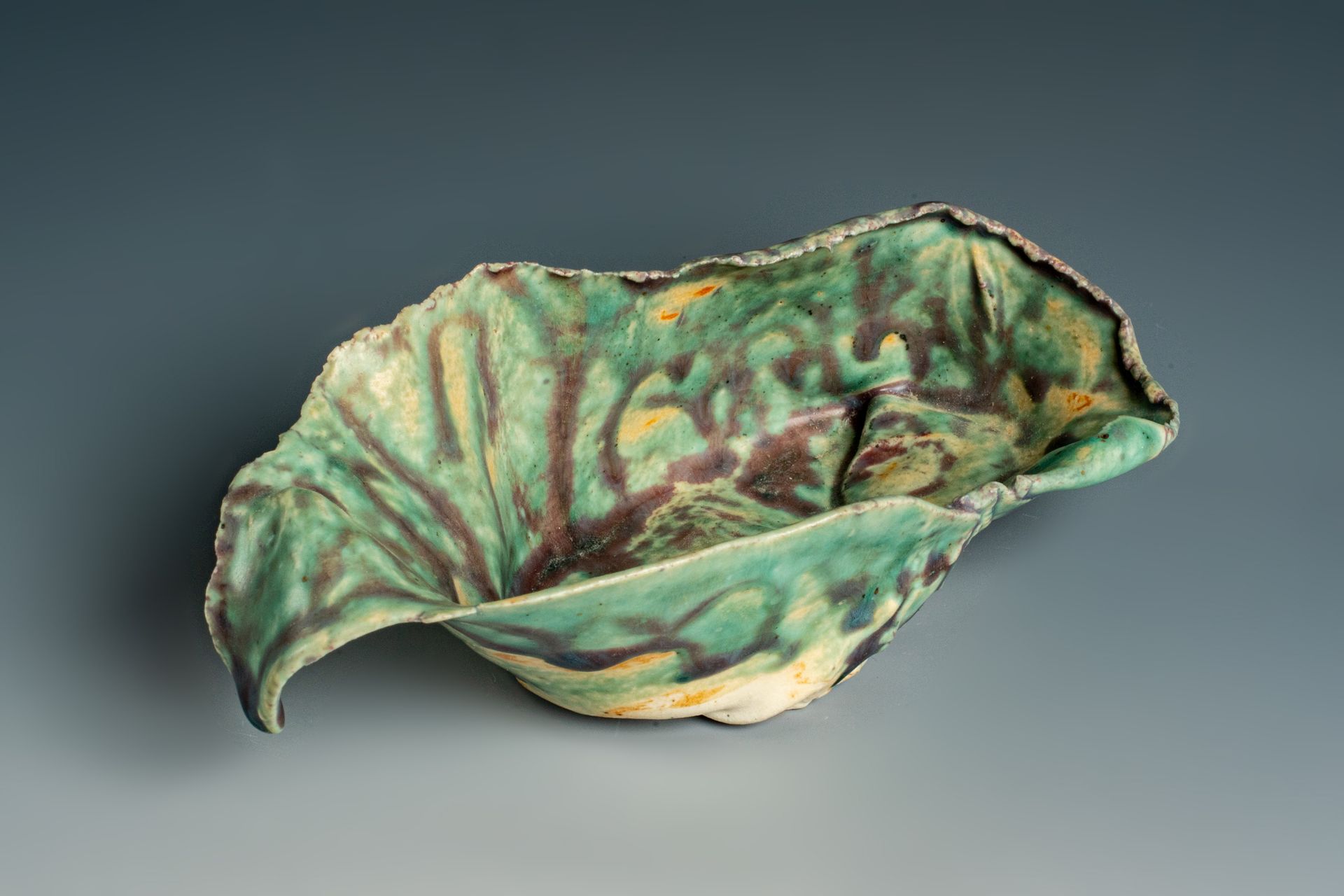 A green leaf shaped bowl is sitting on a gray surface.
