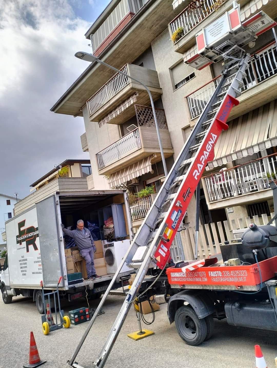 Un camion in movimento con una scala attaccata è parcheggiato davanti a un edificio.