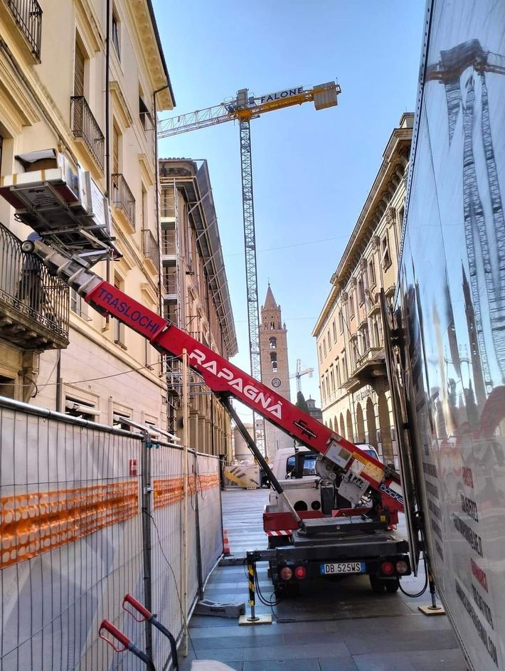 Un camion con una gru agganciata è parcheggiato in uno stretto vicolo tra due edifici.