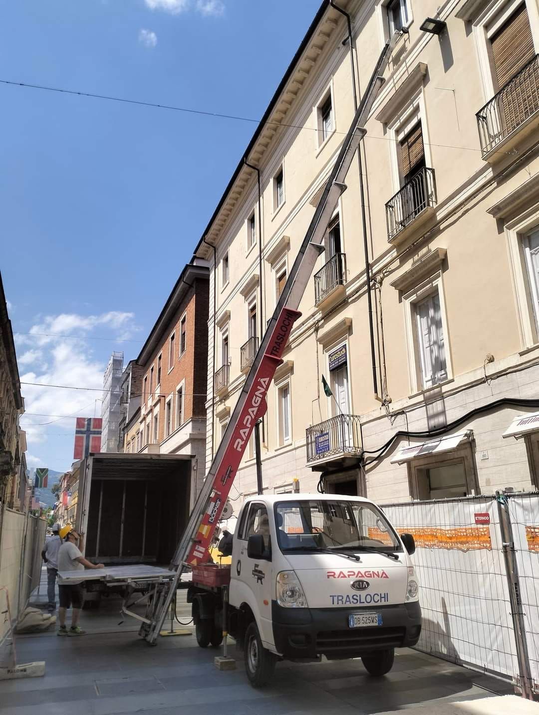 Un camion con una gru agganciata è parcheggiato davanti a un edificio.
