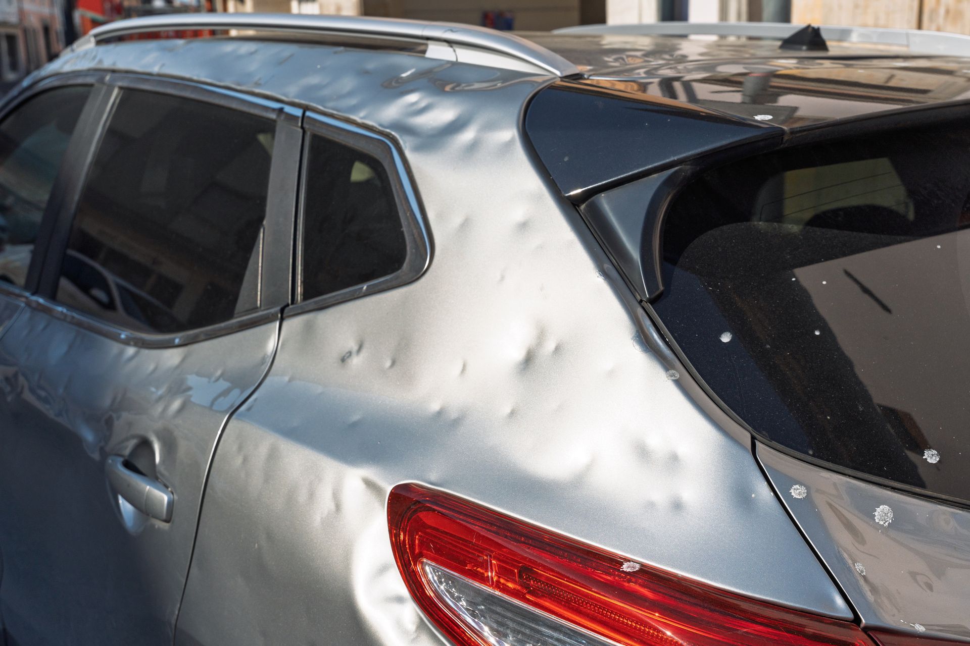 Silver SUV with multiple dents across the rear side panel caused by hail damage, showing the need fo