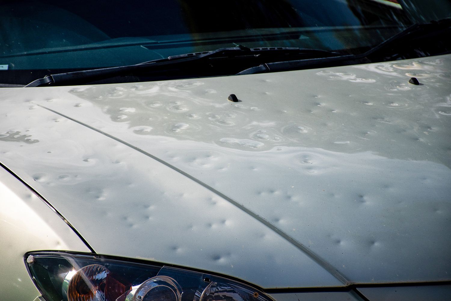 Car hood covered in hail damage dents beneath the windshield.