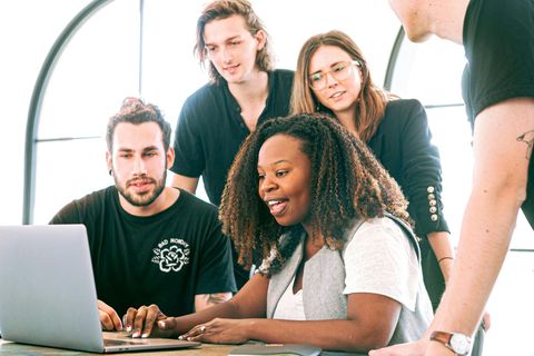 Group of people working on a laptop in a modern office, smiling and discussing ideas.