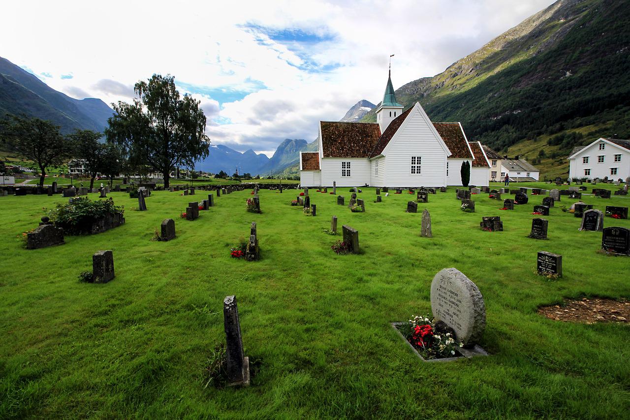 Grassy cemetery with white church and mountains under a cloudy sky