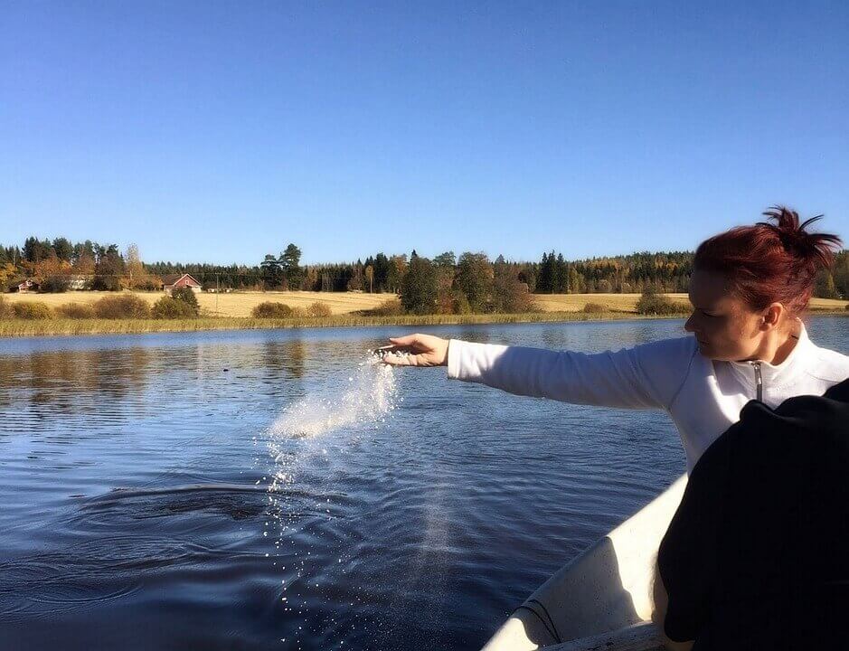 Person on a boat splashes water into a calm lake under a clear blue sky