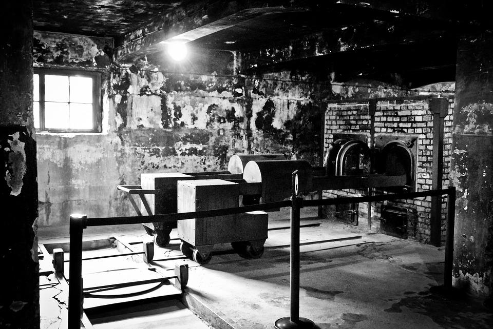 Dim, abandoned brick room with peeling walls, a single window, and old machinery behind a railing.