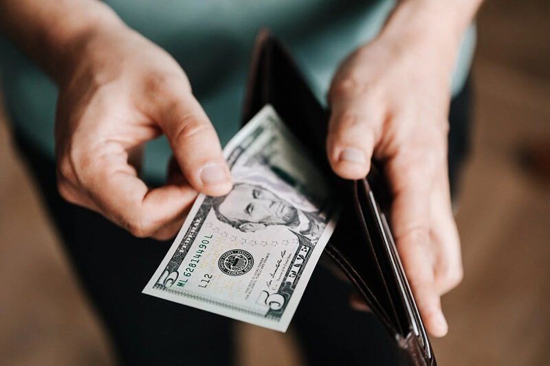 Hands pulling a dollar bill from an open brown wallet