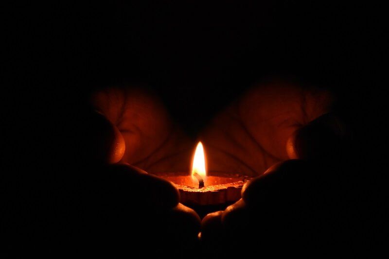 A lit candle glowing in cupped hands against a dark background