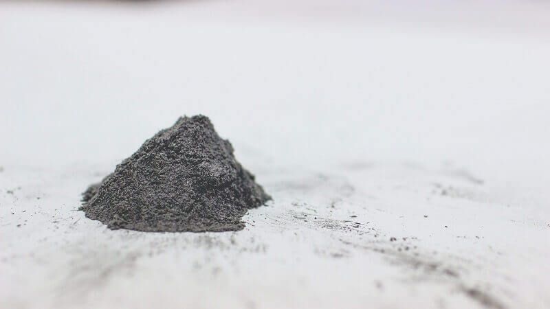 Small pile of dark gray powder on a white marble surface with a few scattered granules.