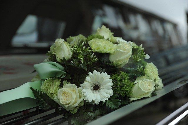 White and green floral bouquet on a car hood, likely for a wedding, with a mint ribbon.