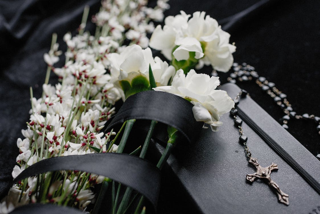 White flowers and a black ribbon on a black coffin with a silver cross necklace