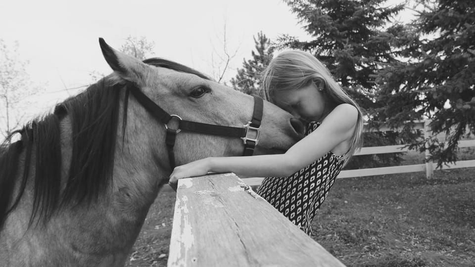 Girl embracing a horse's head over a fence; black and white photo.