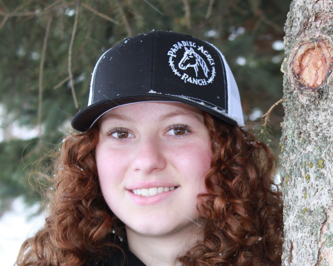 Smiling person in a black cap beside a tree outdoors in winter