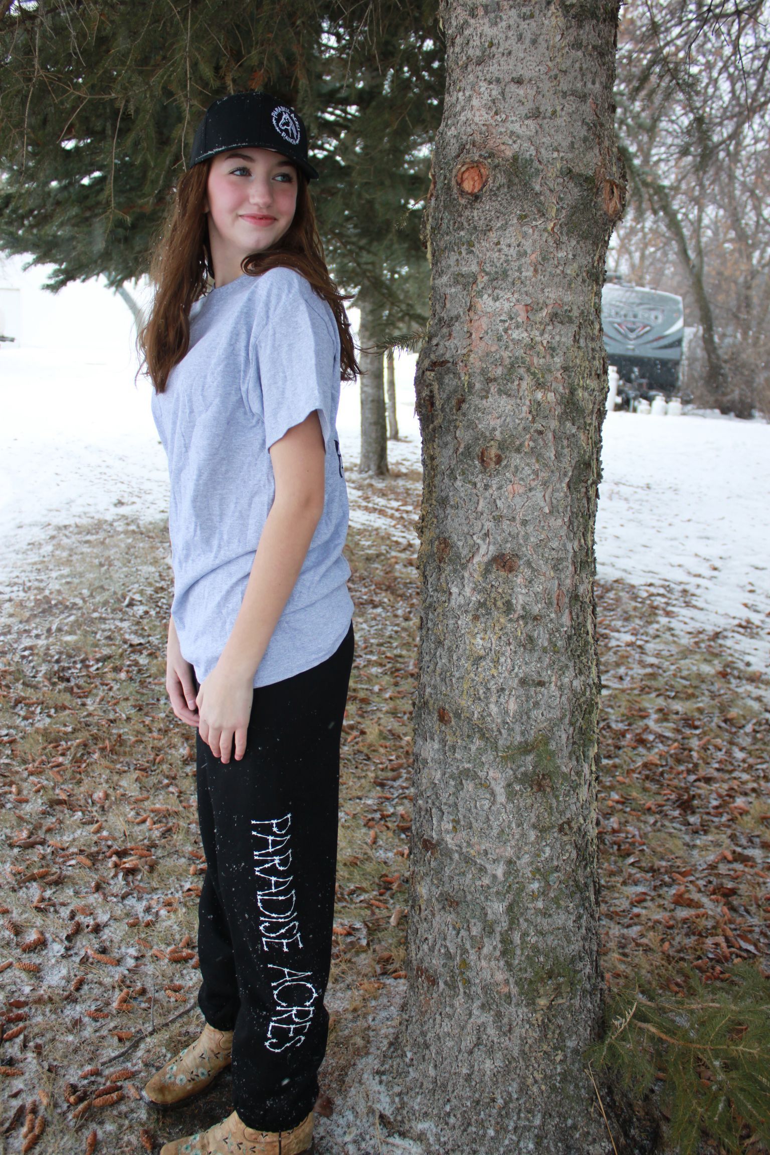 Person walking away on a snowy path, wearing a black cap, gray T-shirt, and black pants.