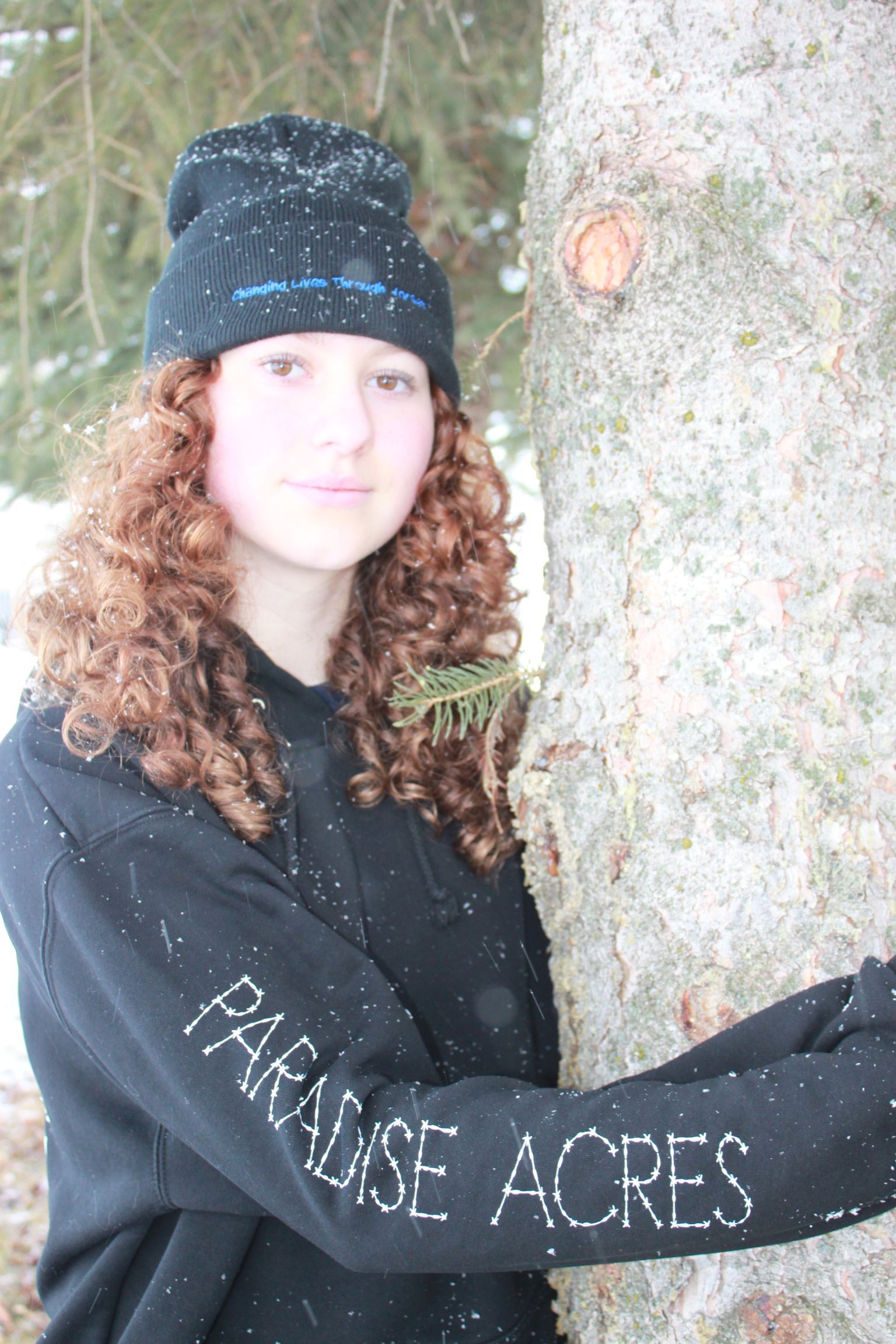 Person in black sweatsuit and hat walks a tan horse in a snowy field.