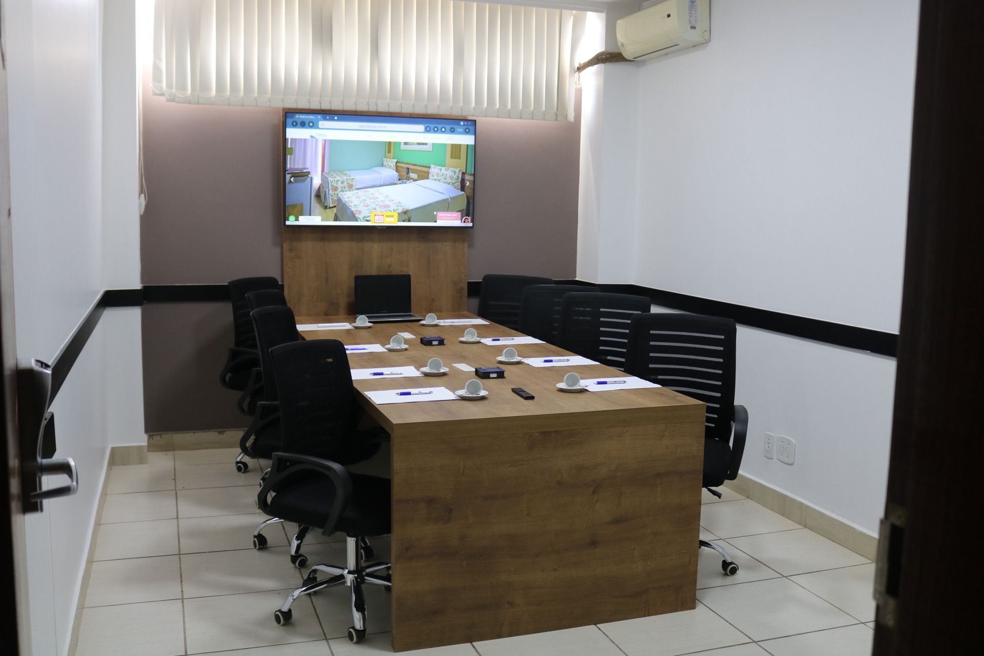 Uma sala de conferências com uma mesa longa, cadeiras e uma TV de tela plana na parede.