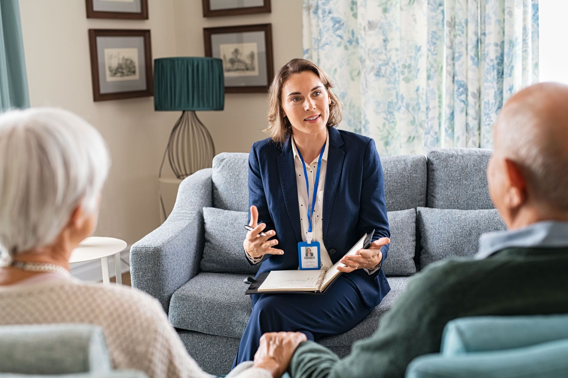 A woman in a blazer consults with an elderly couple on a couch.