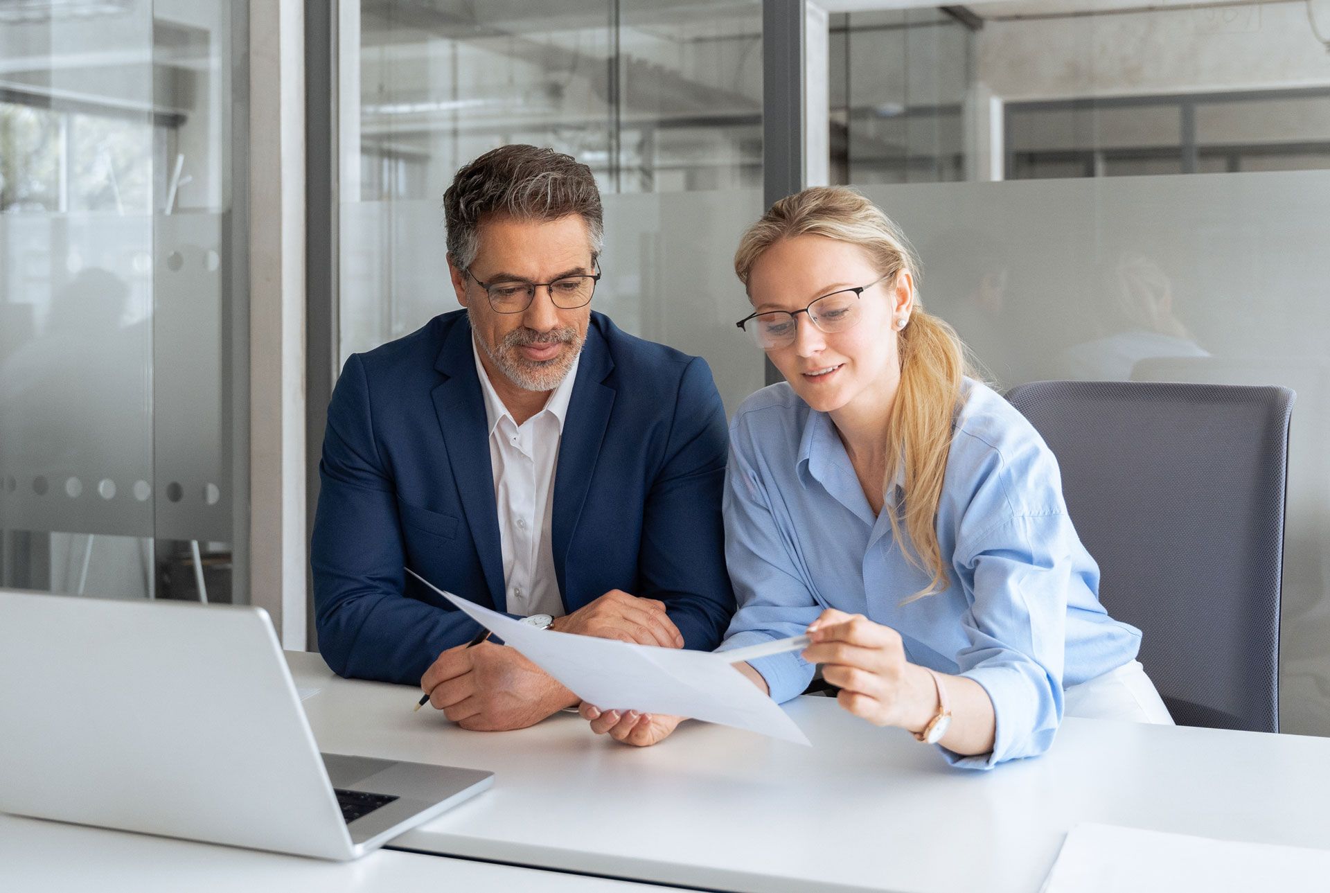 Man and woman in office looking at document, near a laptop.