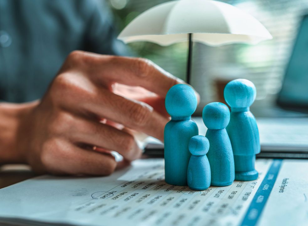Hand holding a miniature umbrella over a wooden family.