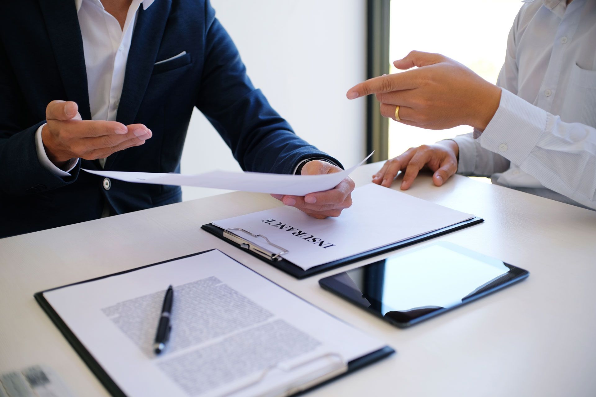 Two people in business attire review documents at a desk, one pointing, with papers and a tablet.