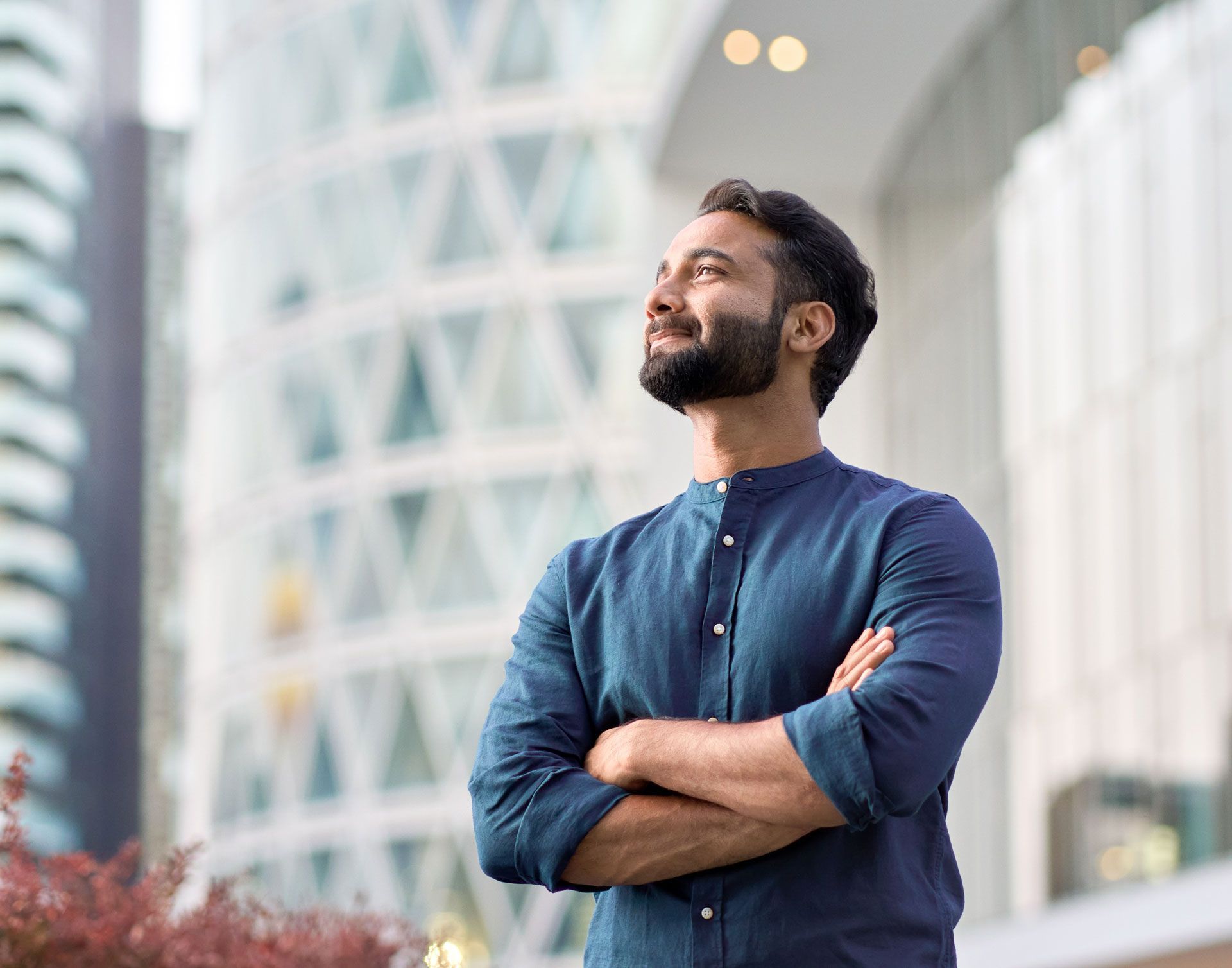 Man with crossed arms looks upward in front of a modern building.