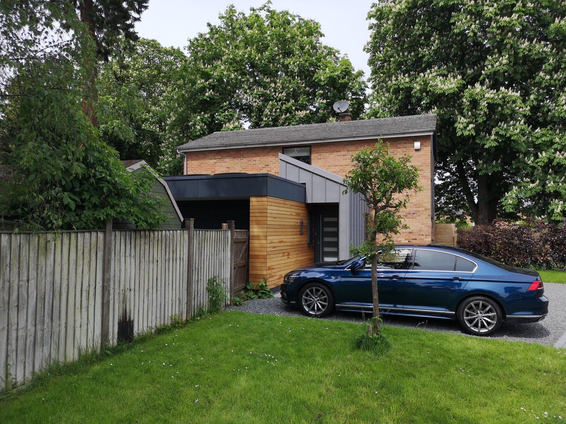 A blue car is parked in front of a brick house.