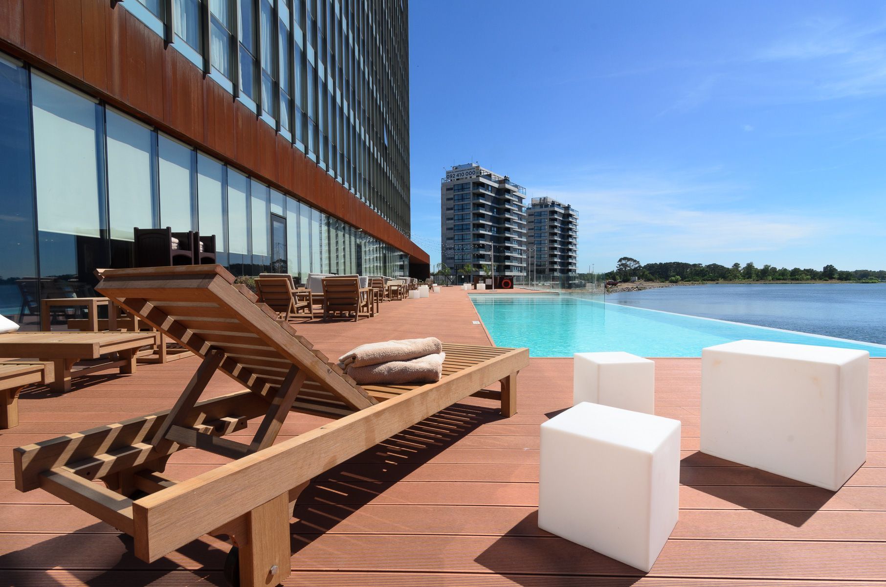 Una terraza de madera con sillas y una piscina al fondo.