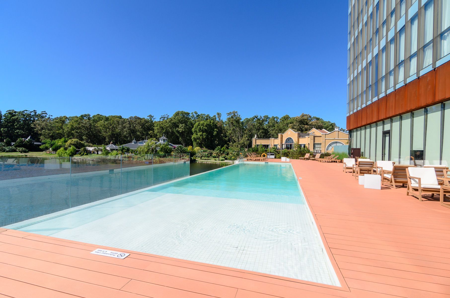 Una gran piscina rodeada de sillas y mesas frente al lago.
