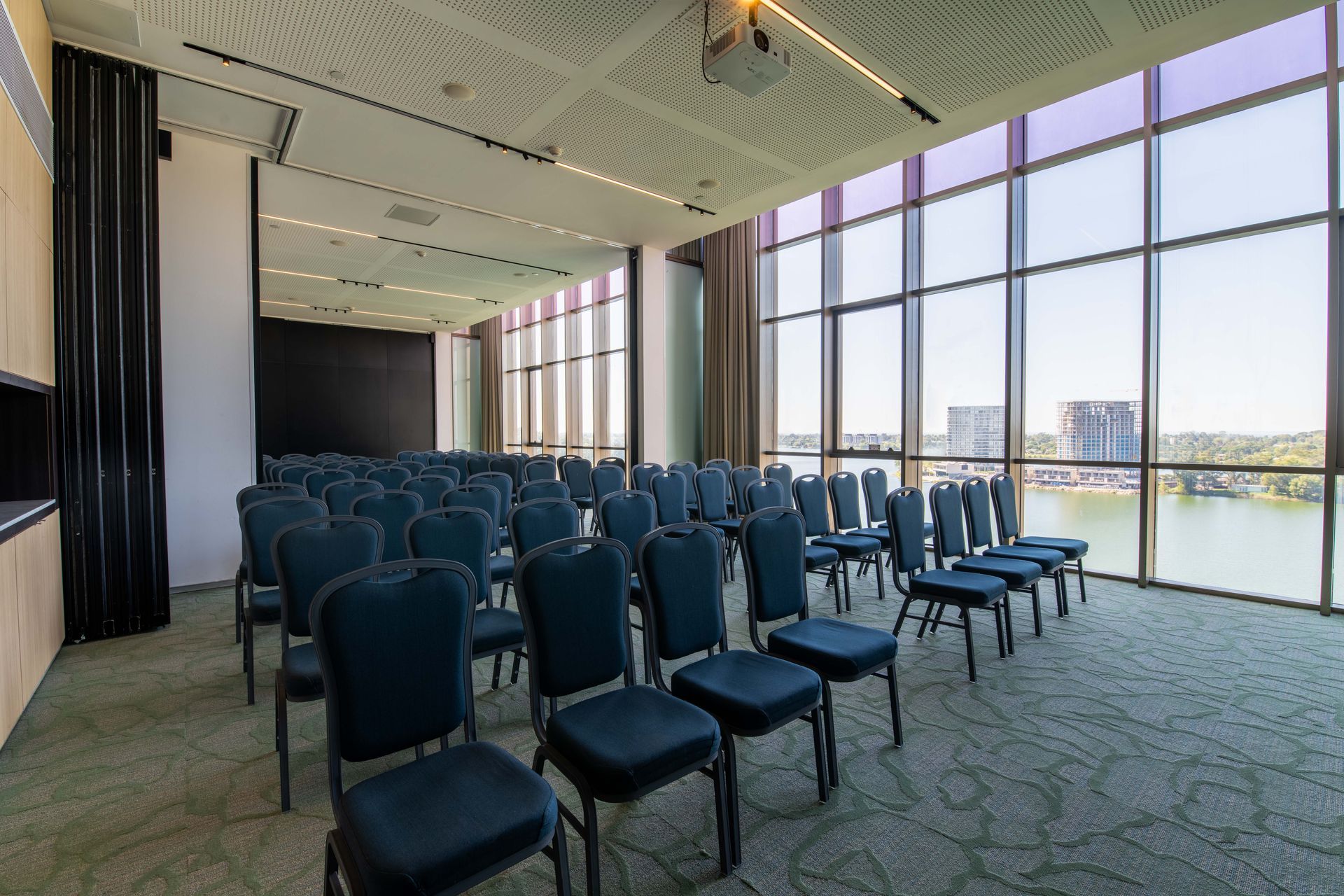 Una sala de conferencias con hileras de sillas y un gran ventanal con vista a un cuerpo de agua.
