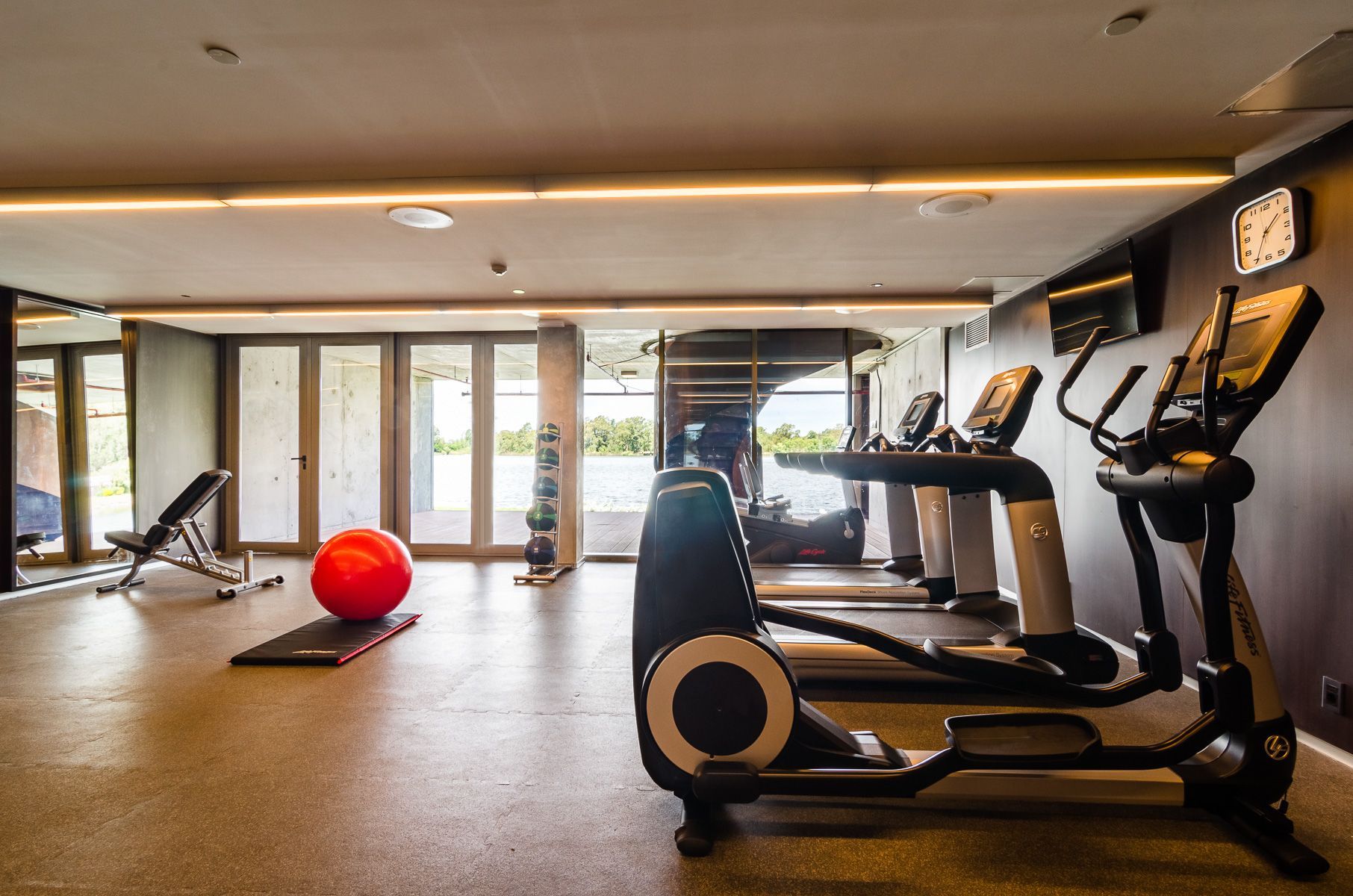 Un gimnasio con cintas de correr, bicicletas estáticas y una pelota roja.