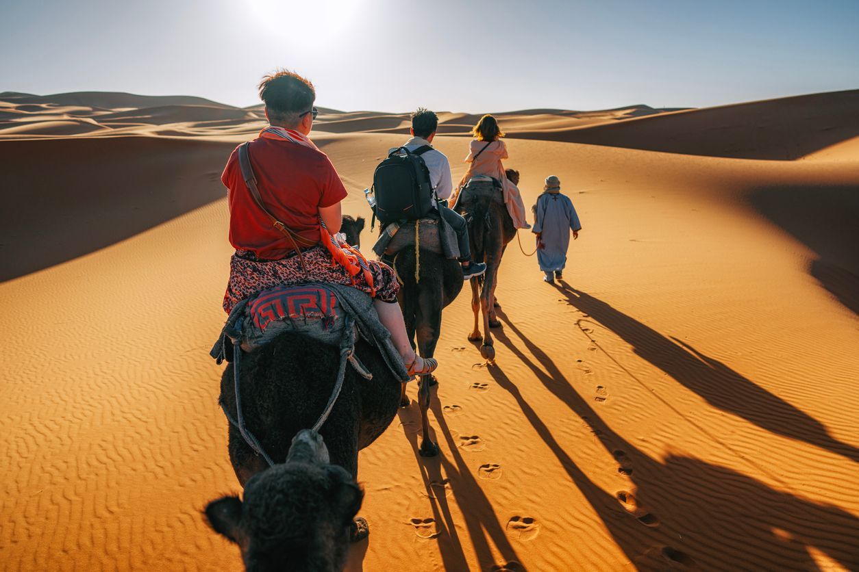 a group of people are riding camels through the desert .