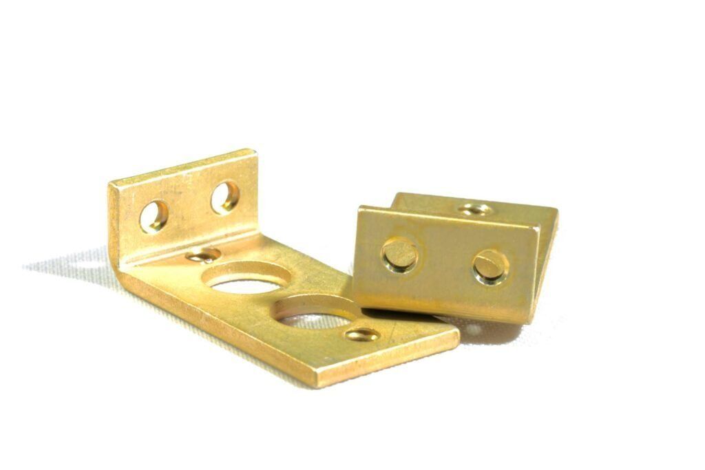 Two brass brackets are sitting on top of each other on a white surface.