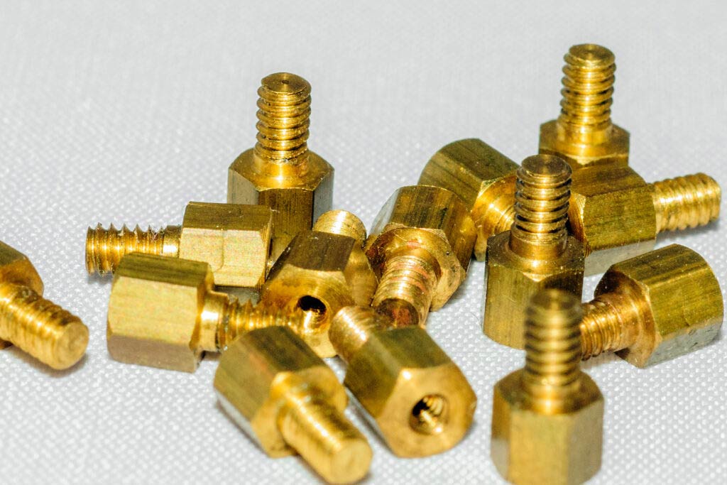 A pile of brass nuts and bolts on a white surface