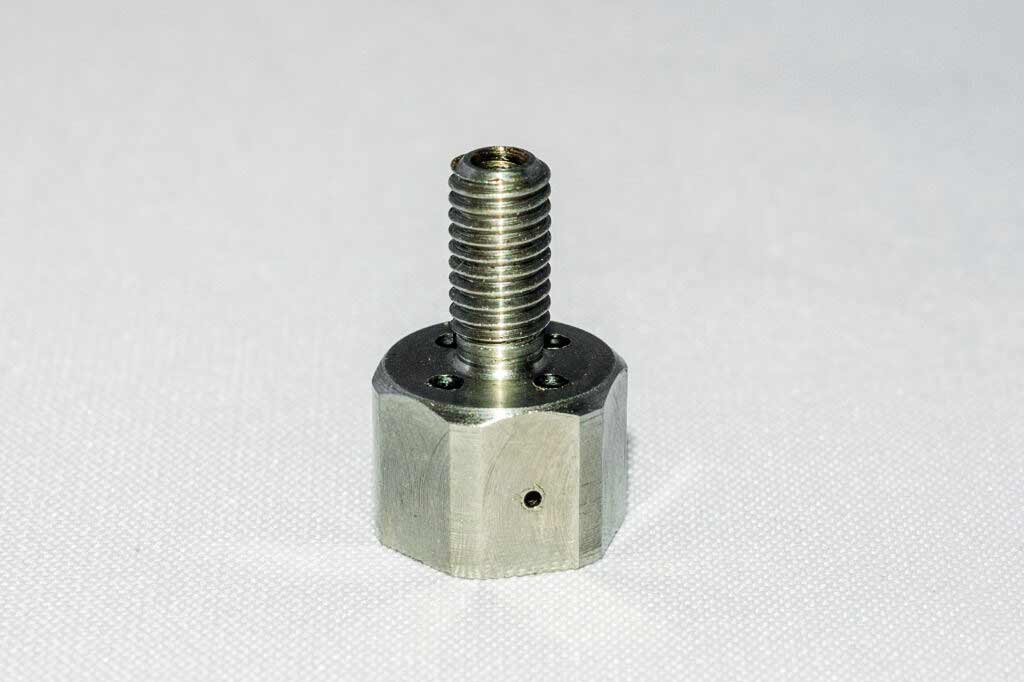 A stainless steel screw with a hole in the middle is sitting on a white surface.