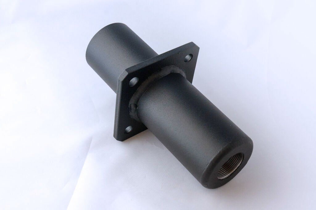 A black metal pipe with holes in it is sitting on a white surface.