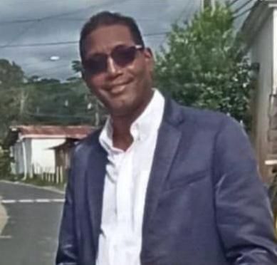 Un hombre con traje y gafas de sol está parado al costado de la carretera.