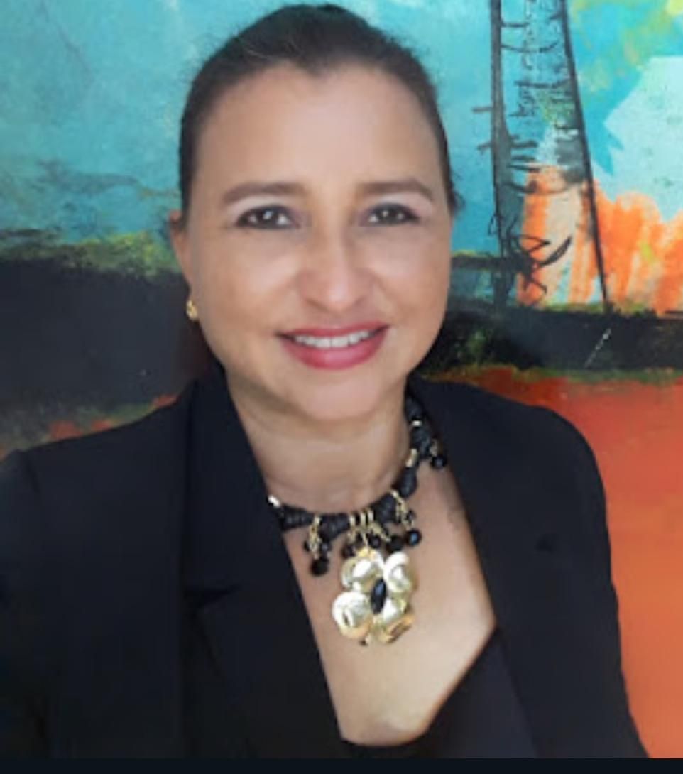 Una mujer con una chaqueta negra y un collar sonríe frente a un cuadro.