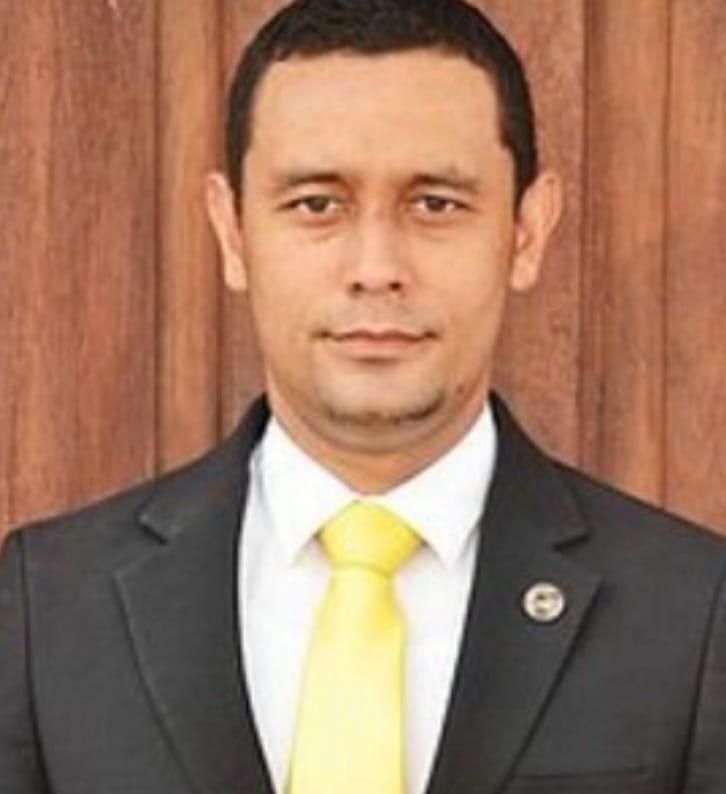 Un hombre con traje y corbata está parado frente a una pared de madera.