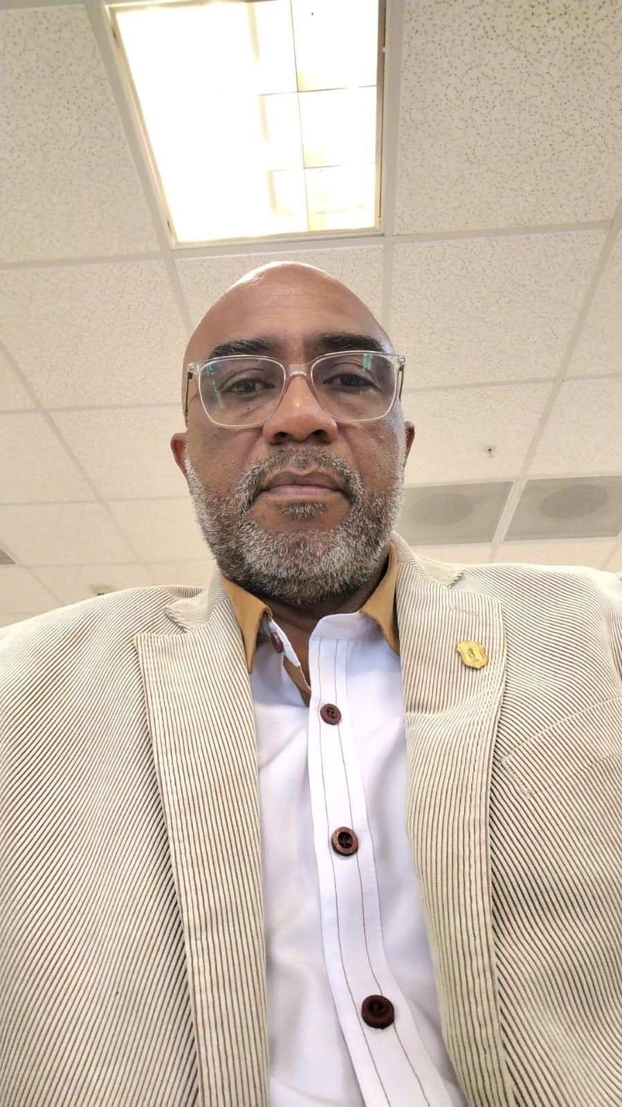 Un hombre con traje y gafas está sentado en una silla.