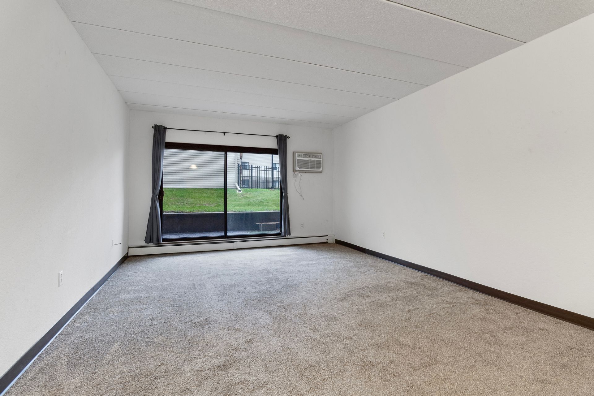 An empty living room with a sliding glass door and a window.