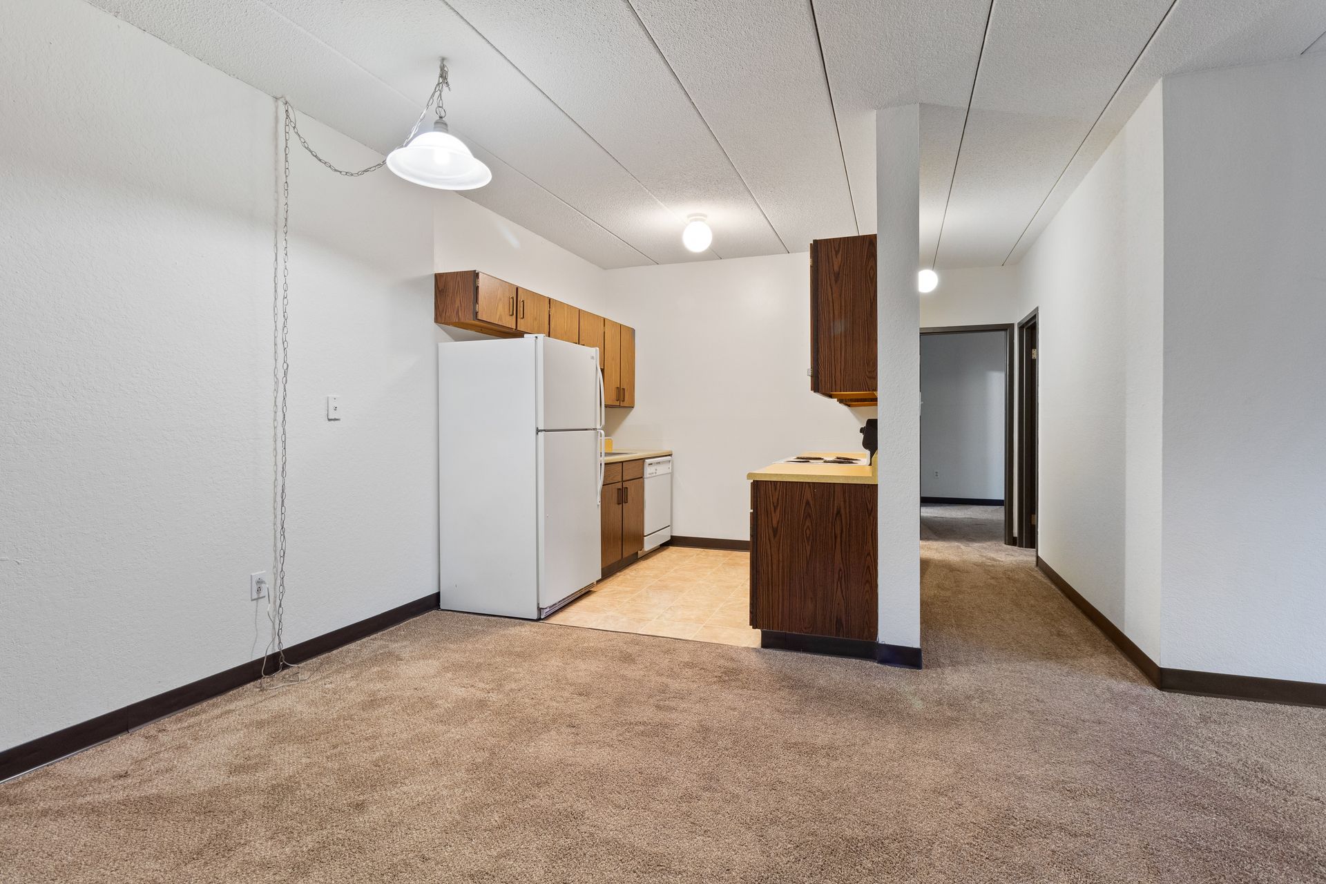 An empty room with a kitchen and a refrigerator in it.