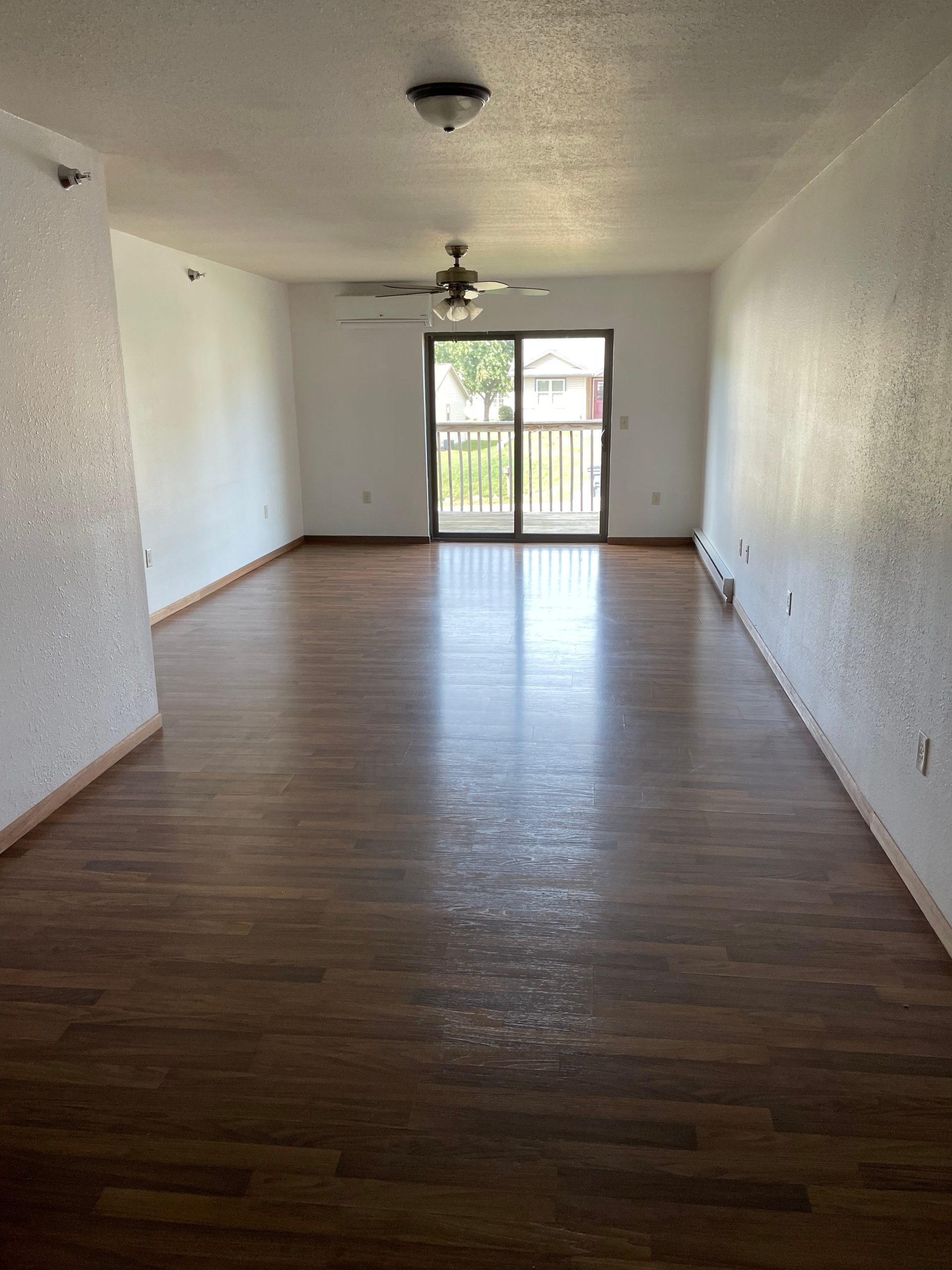 An empty living room with hardwood floors and a ceiling fan.