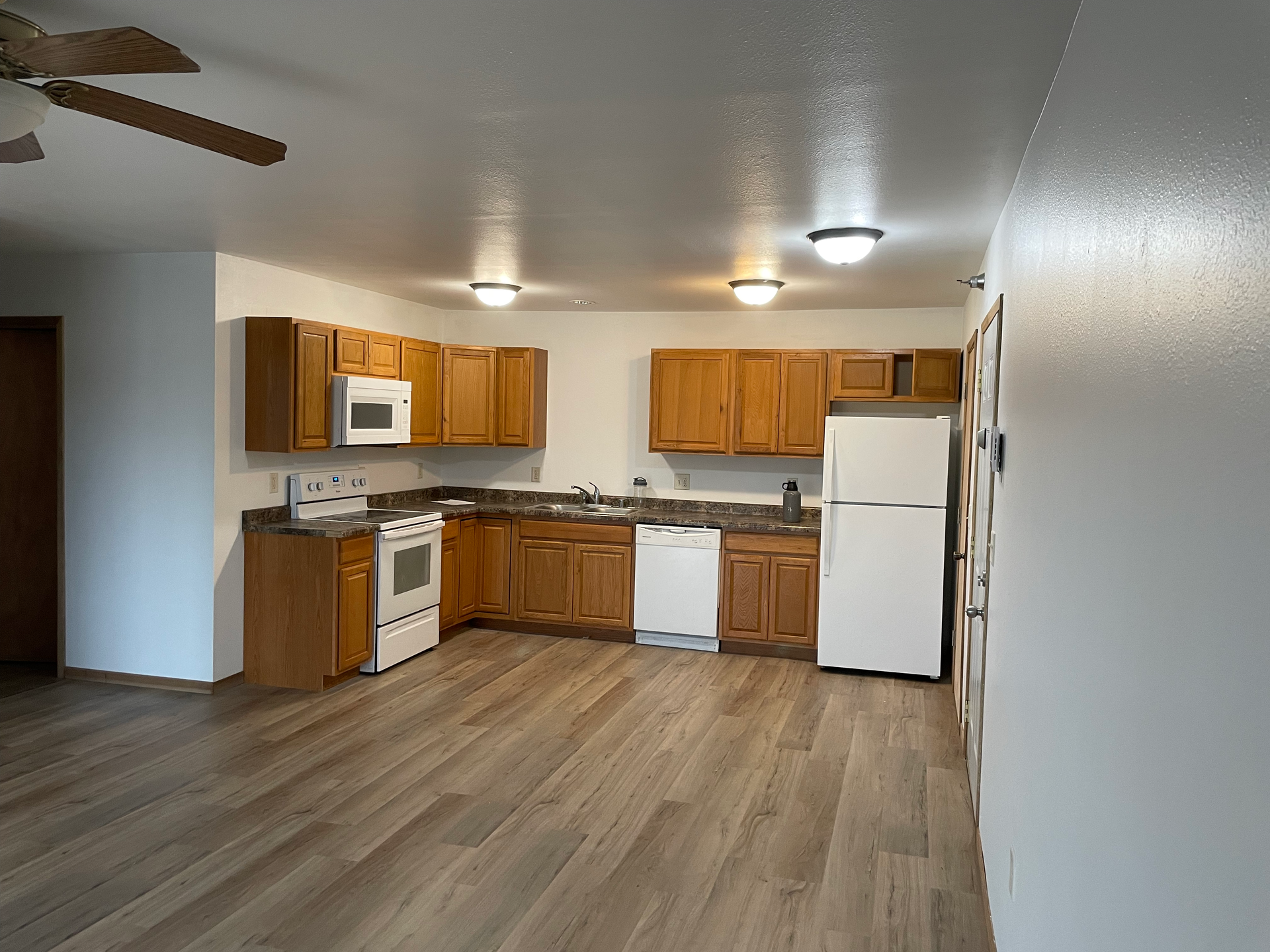 A kitchen with wooden cabinets , a refrigerator , a microwave , and a ceiling fan.