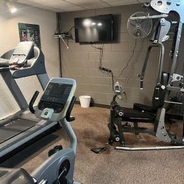 A gym with a treadmill , exercise bike , and television.