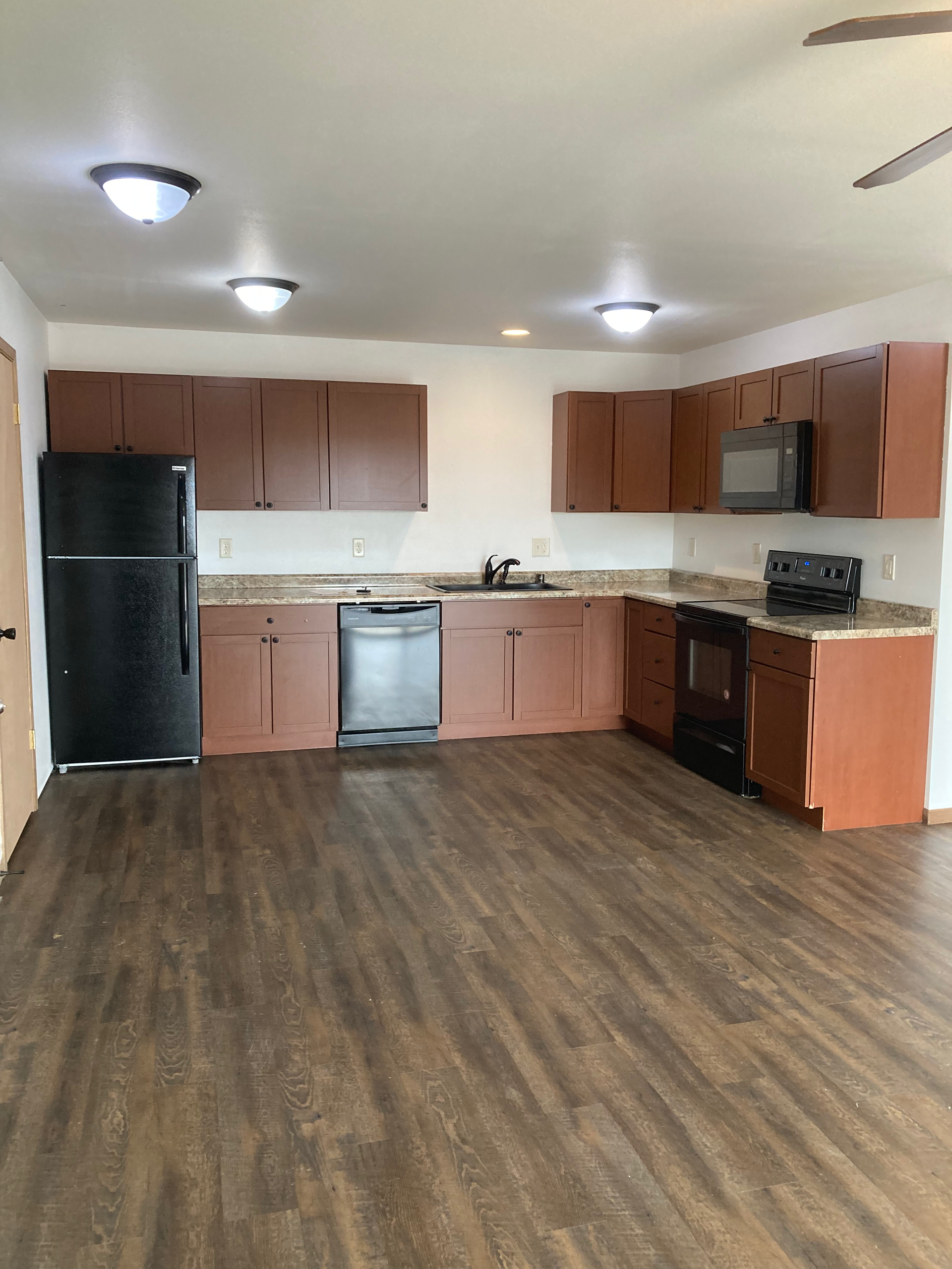 An empty kitchen with wooden cabinets and a black refrigerator