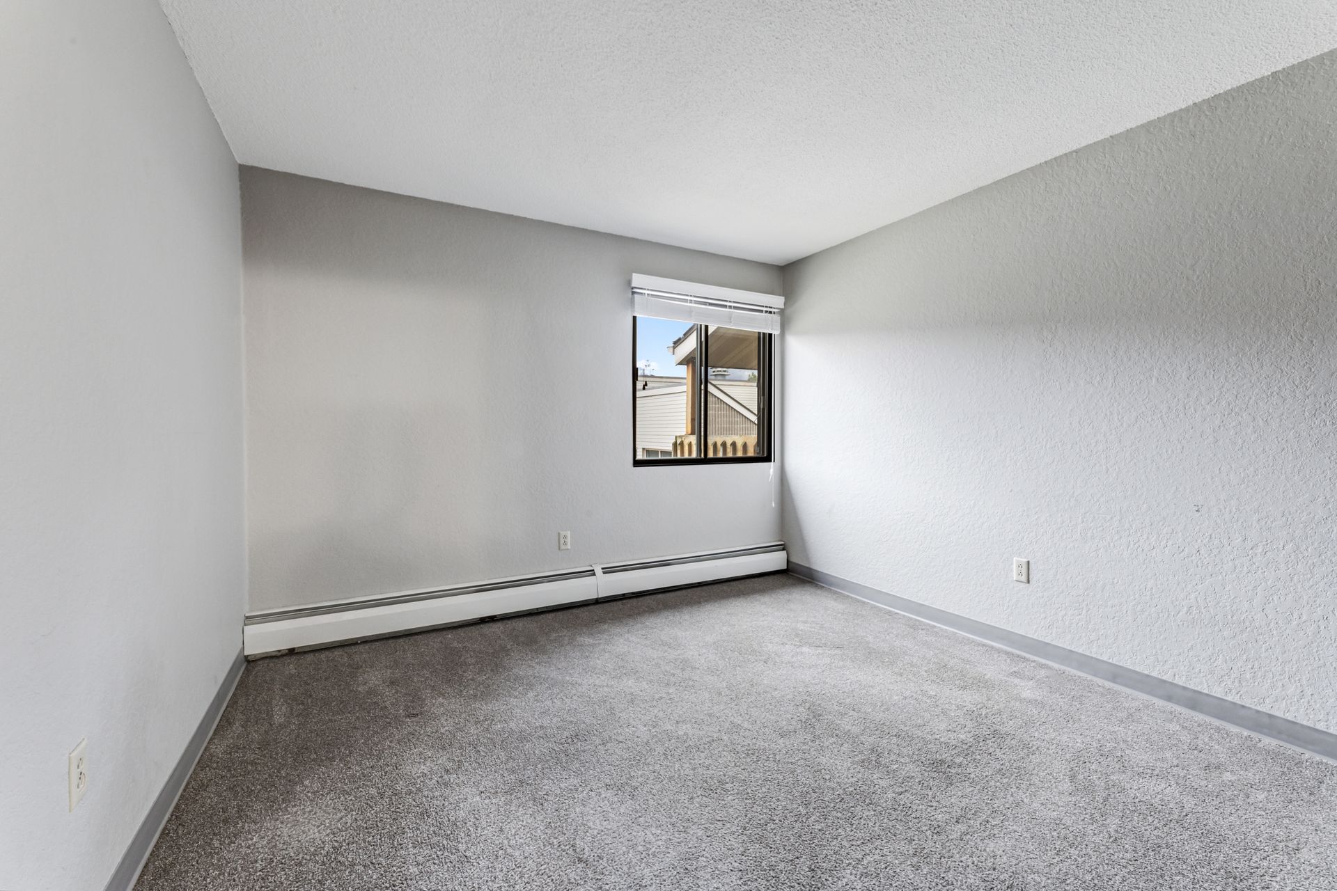 An empty bedroom with a window and a gray carpet.