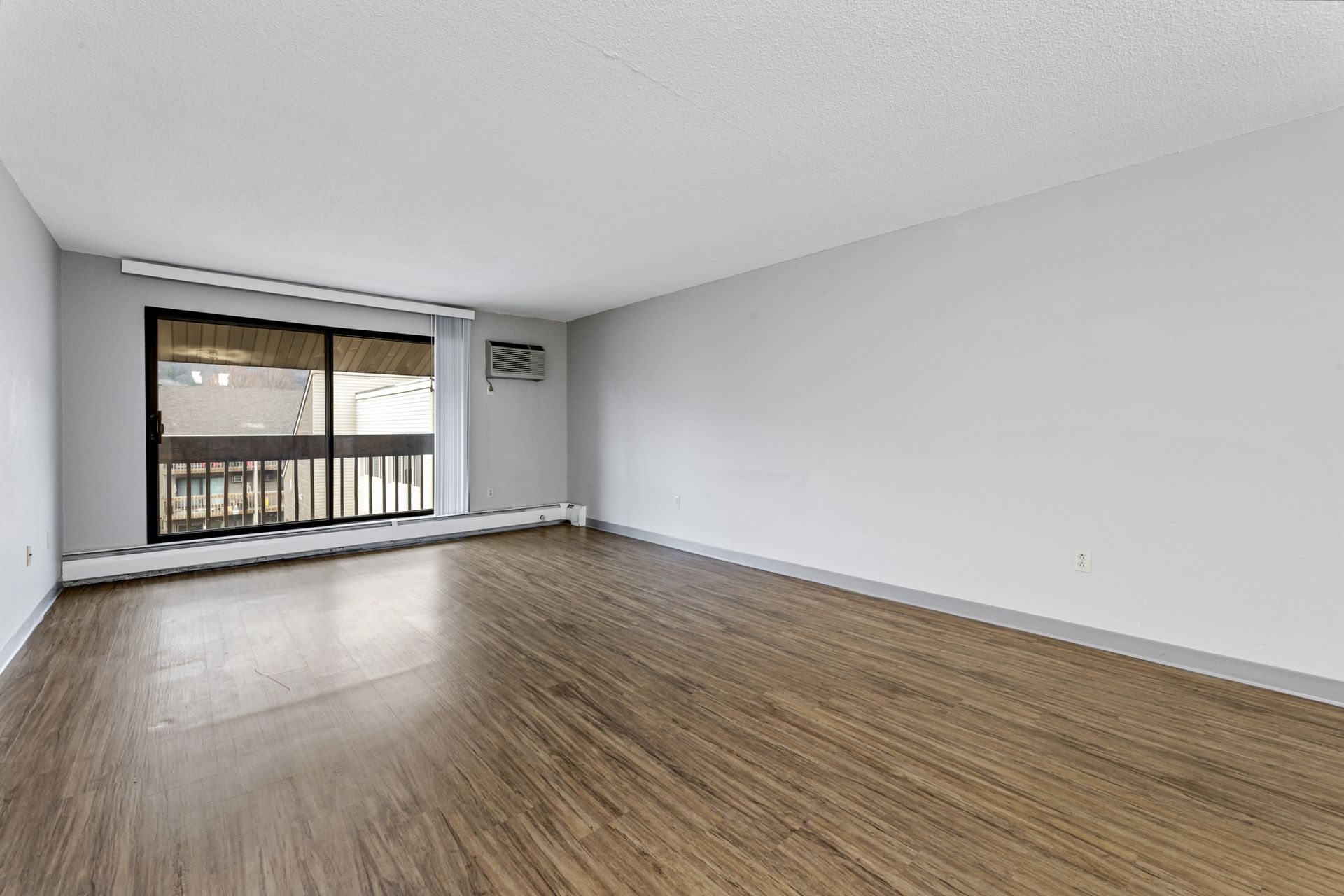 An empty living room with hardwood floors and a balcony.