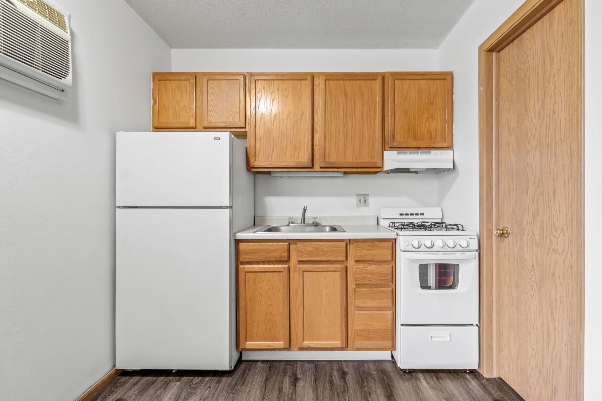 A small kitchen with a refrigerator , stove , sink and cabinets.